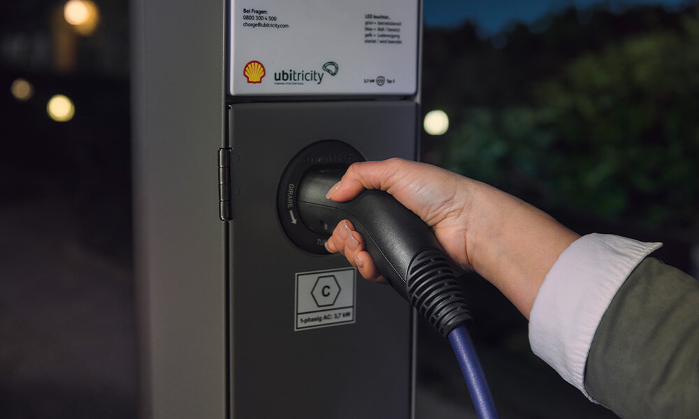 Person holding a charging cable in street in front of car