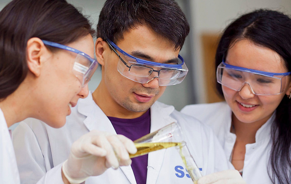 People with goggles and lab coats pouring a solution into a test tube